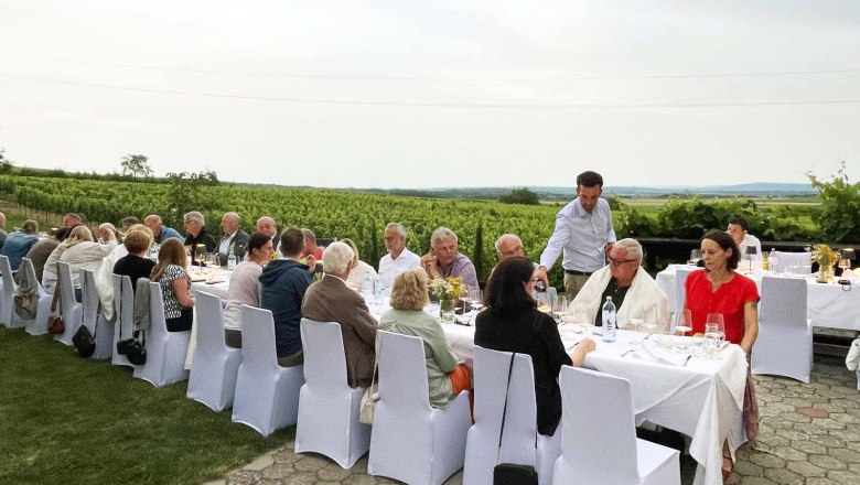 Tafeln im Weinviertel, © Weinviertel Tourismus GmbH Menschen sitzen an einem langen Tisch im Freien, umgeben von Weinbergen.
