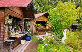 Keramik Slama, © Weinstraße Weinviertel Garten mit Holzhütten, Pflanzen und Keramikdekorationen.