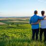 Sanfthügelige Weinlandschaft, © Tonality Ein Paar steht umarmt auf einem Hügel und blickt auf eine weite Weinlandschaft bei Sonnenuntergang.