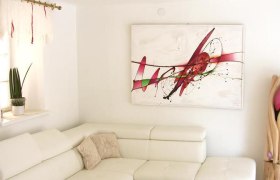 Ferienhaus Schneider, © Schneider Modernes Wohnzimmer mit weißem Sofa, abstraktem Kunstwerk an der Wand und dekorativer Pflanze.