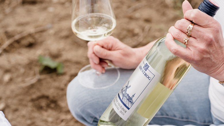 Weingut Ladentrog, © Stefan Jurecek Person hält eine Flasche Weißwein und ein Weinglas in der Hand.