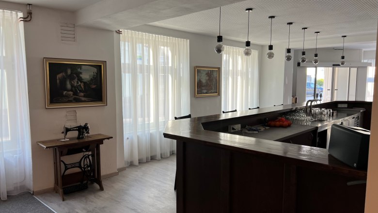 Barbereich, © Balcar Ein moderner Barbereich mit dunkler Holztheke, hängenden Glühbirnen und einer alten Nähmaschine auf einem Tisch.