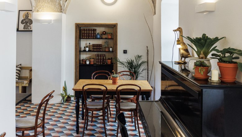 Cafe, © oldrichhrb Ein stilvolles Café mit gewölbter Decke, buntem Fliesenboden, Holztisch und Stühlen. Ein Klavier steht rechts, Pflanzen und Dekorationen sind verteilt.