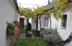 Innenhof, © Familie Ackerl Ein gemütlicher Innenhof mit Holztisch und Bänken, umgeben von weißen Wänden, Blumen und Weinreben.