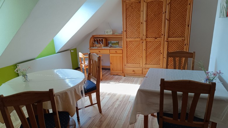 Frühstücksraum, © Kahrer Ein gemütlicher Frühstücksraum mit Holzmöbeln, zwei gedeckten Tischen und einem Schrank unter einer Dachschräge.