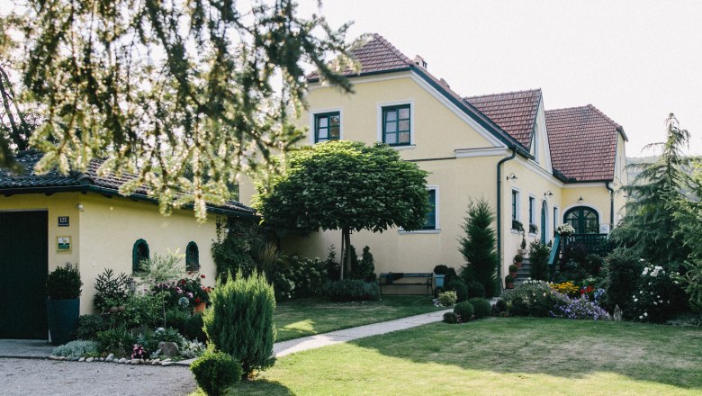 Außenansicht Gästehaus Annemaria, © Agnes Buchmayer Gelbes Haus mit gepflegtem Garten und Bäumen im Vordergrund.
