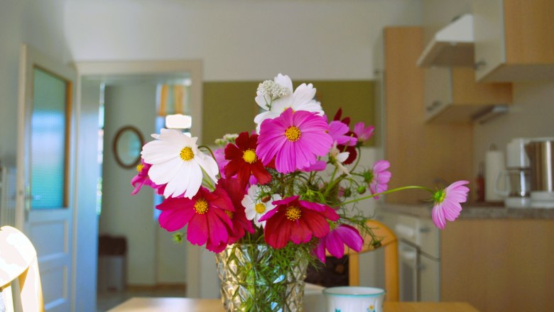 Weinbauernhof Löscher, © Christina Löscher Ein Blumenstrauß mit rosa und weißen Blüten steht in einer Vase auf einem Tisch in einer Küche.