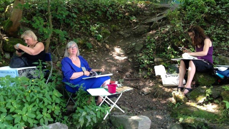 Vernissage Kultur Punkt Hardegg, © Rosi Grieder Drei Frauen sitzen im Freien und zeichnen in einem bewaldeten Gebiet.