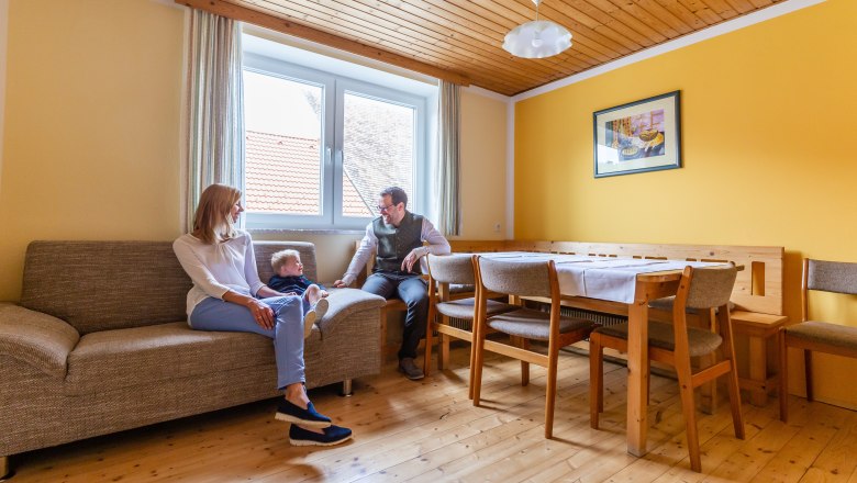 Zimmer, © Andreas Schweighofer Familie sitzt in einem Wohnzimmer mit gelben Wänden und Holzmöbeln.