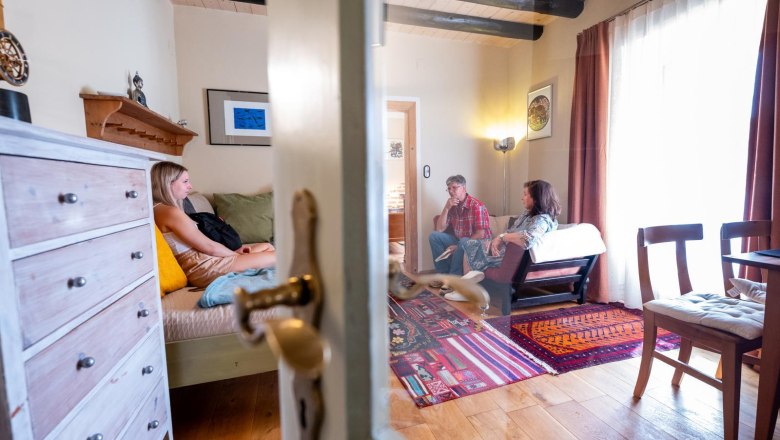 Aufenthaltsraum, © Bernhard Raab Drei Personen sitzen in einem gemütlichen Wohnzimmer mit Holzboden und buntem Teppich.