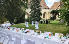 Tafeln im Weinviertel, © Weinviertel Tourismus GmbH Gedeckte Tische im Freien vor einem historischen Gebäude mit Musikern im Hintergrund.