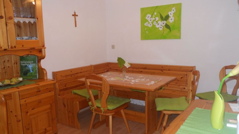 Aufenthaltsraum, © Fam. Döller Gemütlicher Aufenthaltsraum mit Holzmöbeln, Eckbank, Tisch und Dekoration in Grün. An der Wand ein Kreuz und ein Bild mit Blumenmotiv.