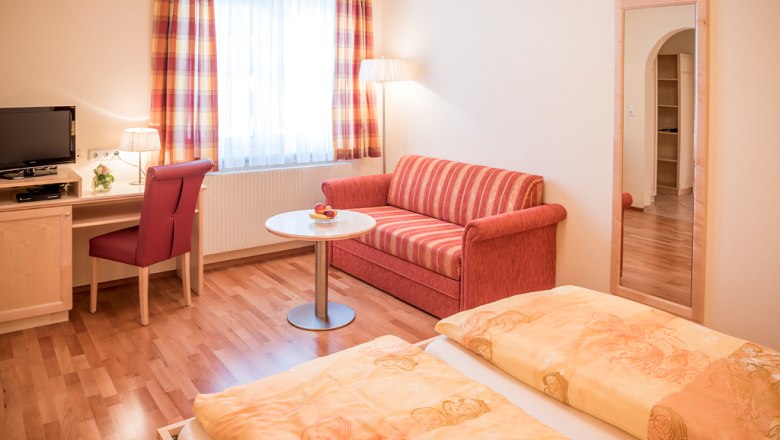 Gästezimmer, © Fam. Breitenfelder Gemütliches Gästezimmer mit Doppelbett, rotem Sofa, Schreibtisch, Fernseher und großem Spiegel.