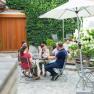 Gemütlicher Innenhof, © Tonality Gruppe von Menschen sitzt an einem Tisch in einem begrünten Innenhof mit Sonnenschirm.