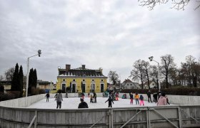 Eislaufplatz in Retz, © Herbert Presler Menschen beim Eislaufen auf einem Freiluftplatz vor einem gelben Gebäude.