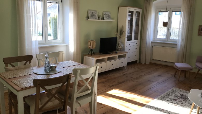 Aufenthaltsraum mit Essbereich, © Martina Braun Heller Raum mit Esstisch, Stühlen, TV-Schrank und großen Fenstern.