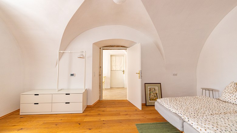 Gewölbezimmer, © Fam. Heichinger Ein Zimmer mit Gewölbedecke, Holzboden, Bett, Kommode und offener Tür.
