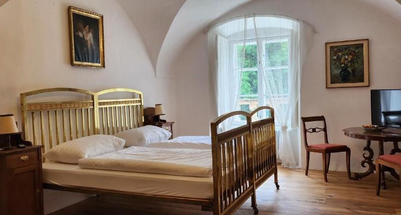 Gästezimmer, © Andrea Schubert Ein gemütliches Gästezimmer mit einem Doppelbett, Holzmöbeln und einem großen Fenster mit Vorhängen.