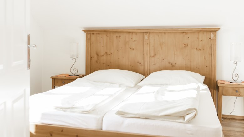 Doppelzimmer, © Agnes Buchmayer Helles Schlafzimmer mit einem Doppelbett aus Holz und weißen Bettlaken.