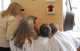 Guckkasten, © Herbert Bednarik Gruppe von Kindern und einer Frau schauen durch Löcher in einer Holzwand.