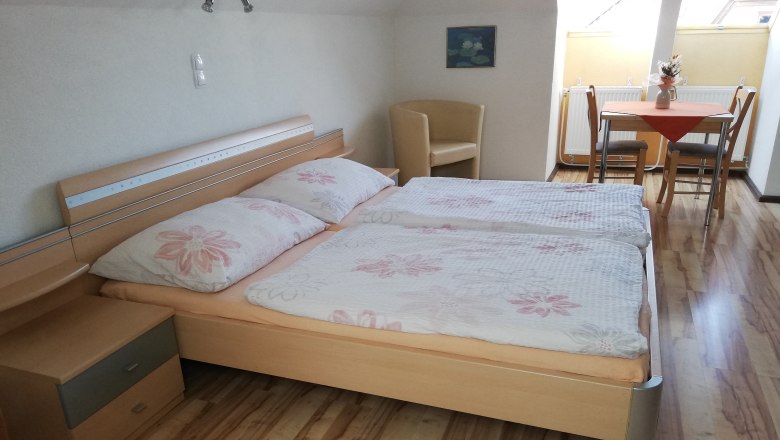 Doppelzimmer, © Kahrer Ein gemütliches Doppelzimmer mit Holzboden, Doppelbett, Nachttisch, Tisch mit Stühlen und Dachfenster.