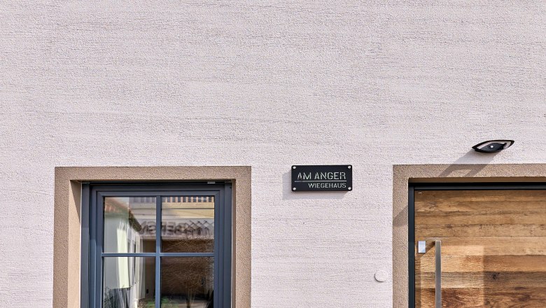 Wiegehaus, © Bernhard Raab Fassade eines modernen Hauses mit einem Fenster und einer Holztür, unter blauem Himmel.
