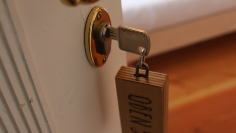 OBENauf, © OBENauf Nahaufnahme eines Türgriffs mit Schlüssel und Holzanhänger mit der Aufschrift 'OBEN 5'.