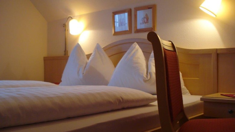 Gästezimmer, © Pension Rudi Gemütliches Gästezimmer mit Doppelbett, zwei Nachttischlampen und einem Stuhl.