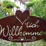 Herzlich Willkommen, © Familie Fleischmann Metallschild mit der Aufschrift 'Herzlich Willkommen' in einem Garten.