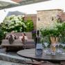 Relaxen am Weingut, © Tonality Ein Tisch mit Weingläsern und Flasche, im Hintergrund zwei Personen auf einer Liege im Garten.