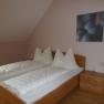 Gästezimmer, © Fam. Seher Ein schlichtes Gästezimmer mit einem Doppelbett, weißen Bettdecken und einem Nachttisch mit Lampe.