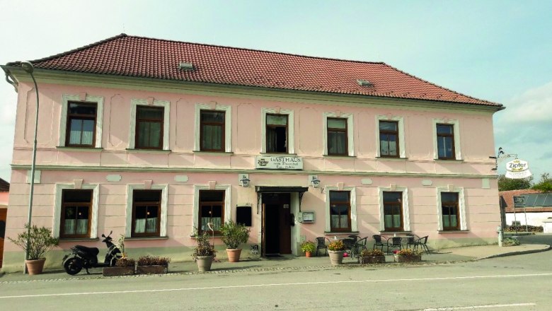 Gasthof zum Thayatal, © Bednarik Herbert Ein zweistöckiges, rosa Gebäude mit einem roten Ziegeldach und mehreren Fenstern. Vor dem Gebäude stehen Pflanzen und ein Motorrad.