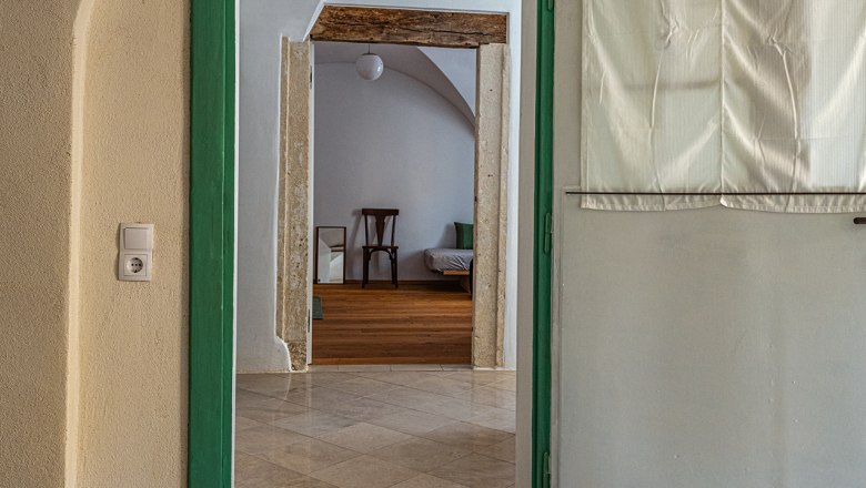Zugang zum Gewölbezimmer, © Fam. Heichinger Blick durch eine geöffnete Tür in ein Gewölbezimmer mit Holzboden und einem Stuhl.