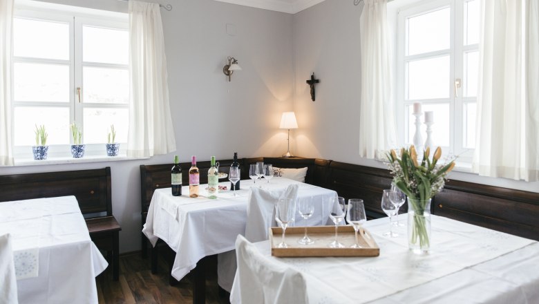 Frühstücksraum, © Agnes Buchmayer Gemütlicher Gastraum mit Holzmöbeln, gedeckten Tischen, Weinflaschen und Blumen.