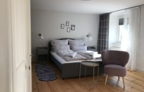 Doppelzimmer, © Martina Braun Modern eingerichtetes Doppelzimmer mit Bett, Sessel und kleinem Tisch auf Holzboden.