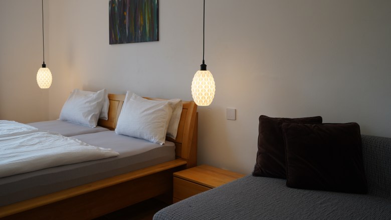 Landhaus Krell, © Weingut Krell Schlafzimmer mit Doppelbett, zwei Hängelampen und einem Sofa mit Kissen.