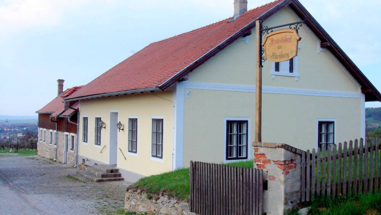Winzerhaus mit gelber Fassade und rotem Dach in l&auml;ndlicher Umgebung.