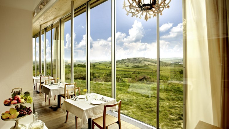 Innenansicht eines Restaurants mit gro&szlig;en Fenstern und Blick auf eine gr&uuml;ne Landschaft.