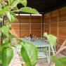 Überdachte Terrasse mit Tisch und Stühlen, umgeben von Holzverkleidung und Pflanzen im Vordergrund.