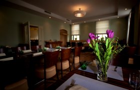 Ein stilvoll eingerichteter Raum mit gedeckten Tischen und einem Blumenstrauß aus lila Tulpen im Vordergrund.