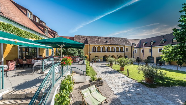 Ein malerischer Innenhof mit gelben Geb&auml;uden, Terrassenbereich und Sonnenschirmen.