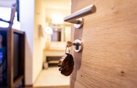 Nahaufnahme einer Holztür mit Schlüssel im Schloss, im Hintergrund ein unscharfer Raum.