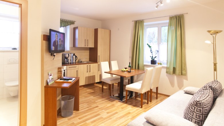 Moderne Küche mit Esstisch, Sofa und Fernseher in einem hellen Raum.