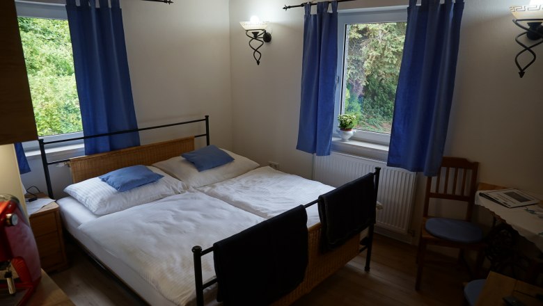 Gem&uuml;tliches Schlafzimmer mit Doppelbett, blauen Vorh&auml;ngen und Holzm&ouml;beln.