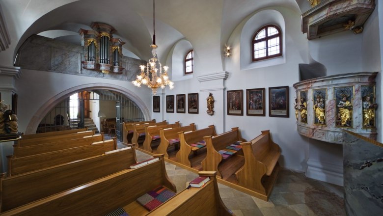 Innenansicht einer kleinen Kirche mit Holzb&auml;nken, einer Kanzel und einer Orgel auf der Empore.