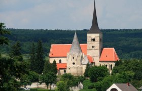 St. Michaelskirche in Pulkau mit rotem Dach und spitzem Turm, umgeben von Bäumen.