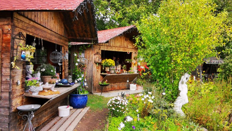 Garten mit Holzhütten, Pflanzen und Keramikdekorationen.