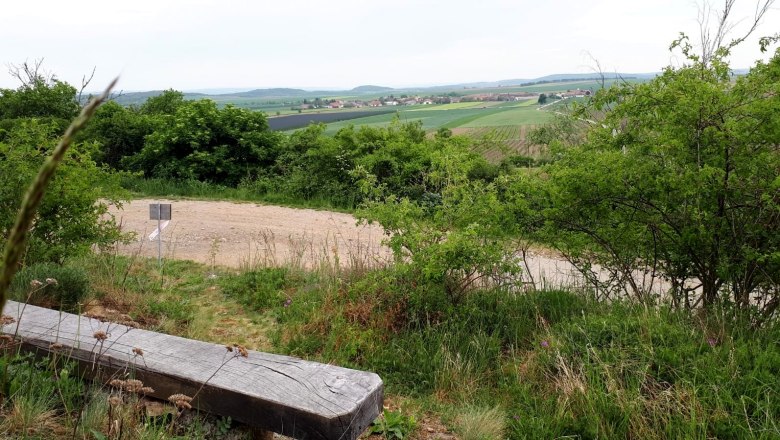 Landschaft mit Bank, Bäumen und Feldern in der Ferne.