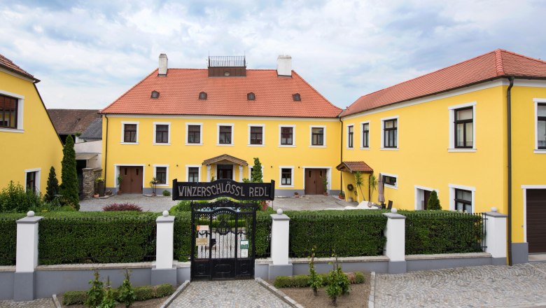 Gelbes Gebäude mit rotem Dach und Tor mit der Aufschrift 'Winzerschlössl Redl'.