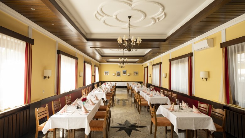 Ein festlich gedeckter Speisesaal mit gelben Wänden, Holzmöbeln und weißen Tischdecken.